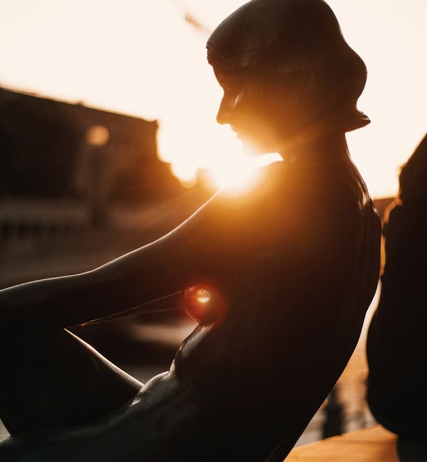 Person sitting in a calm meditation pose, silhouetted against a soft light.